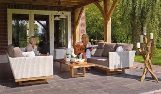 Two women sitting outside on a patio. One woman is playing guitar, and the other is listening and smiling.